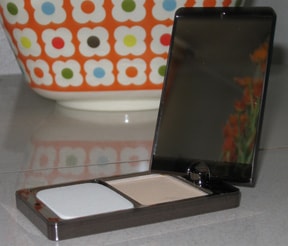 cosmetics package with a phone on a table with an orange bowl