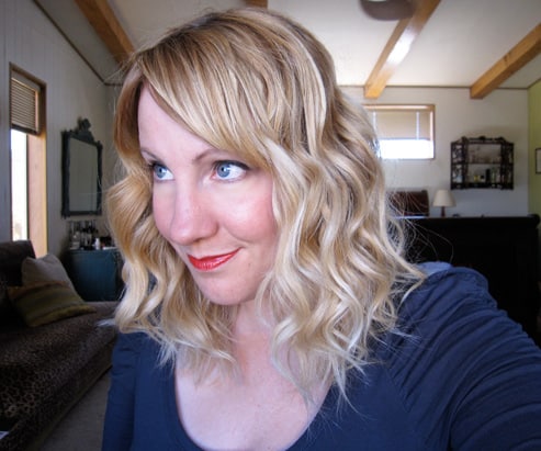 A blonde woman with curls looking at the side smiling 