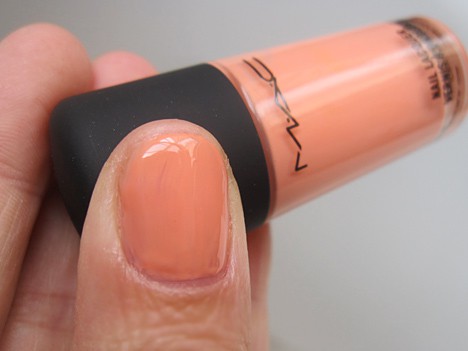 A hand with a creamy apricot shade holding a MAC Nail Lacquer's Play Day with a creamy apricot shade