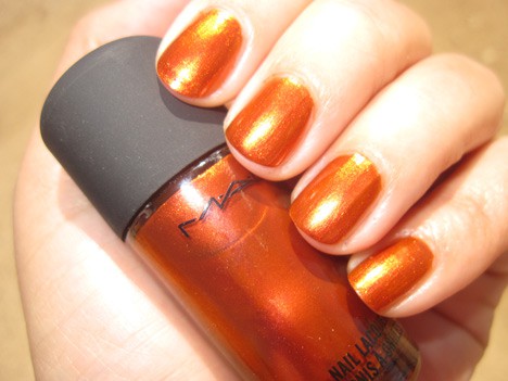 A hand with a orange red duochrome shimmer nail polish holding a nail lacquer of the same color