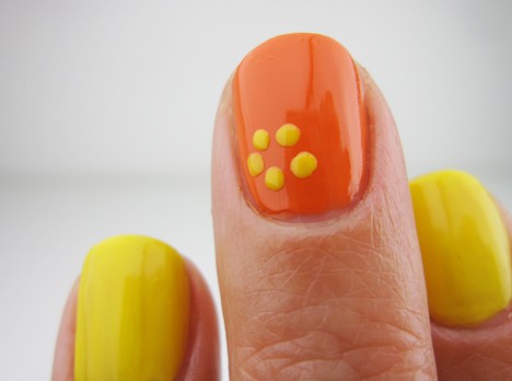 An orange nail polish with 5 dots onto the surface of the nail