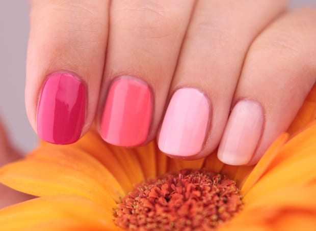 pink shades of essie gel nail polish on woman's finger nails with a yellow flower