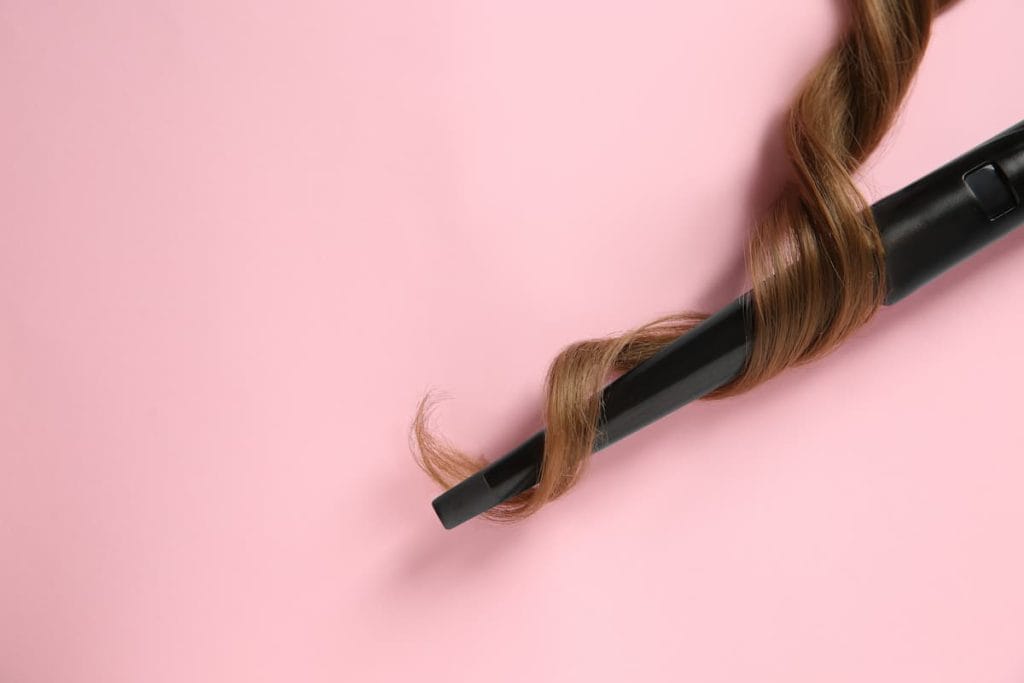 Modern clipless curling iron and brown hair lock on pink background