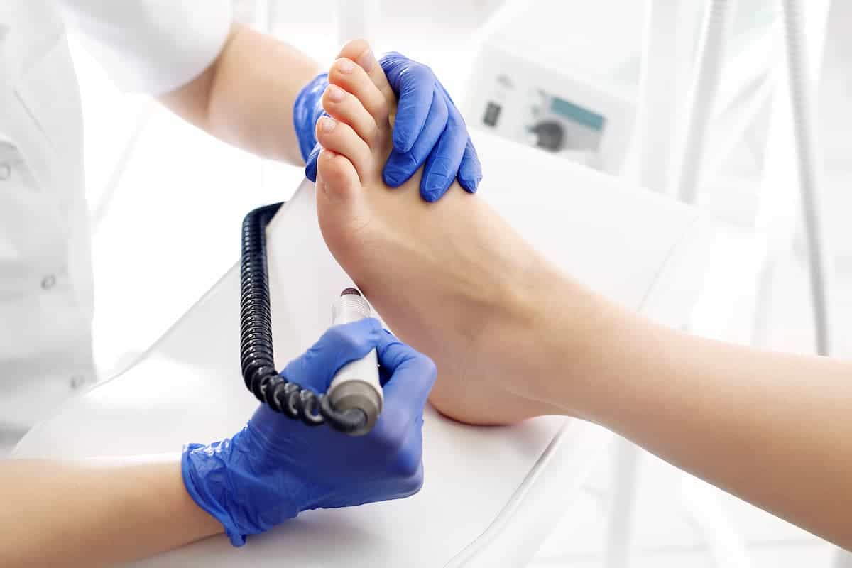 Gloved person using a tool on a foot to give a medical pedicure