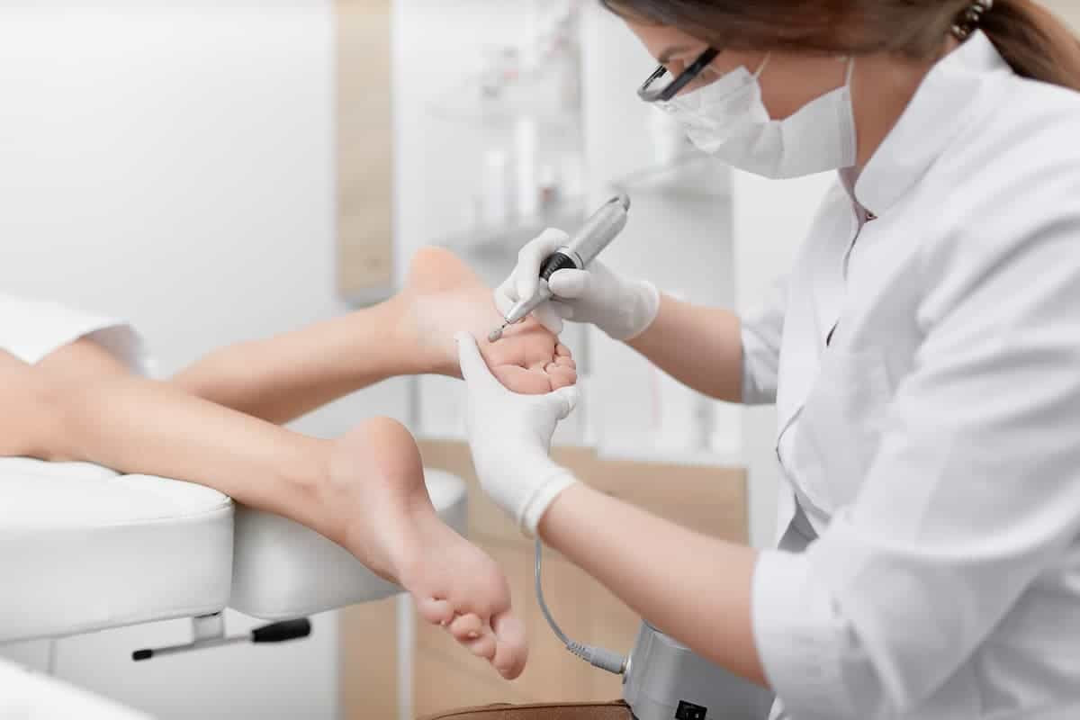 A masked woman using a tool on the bottom of feet during a medical pedicure