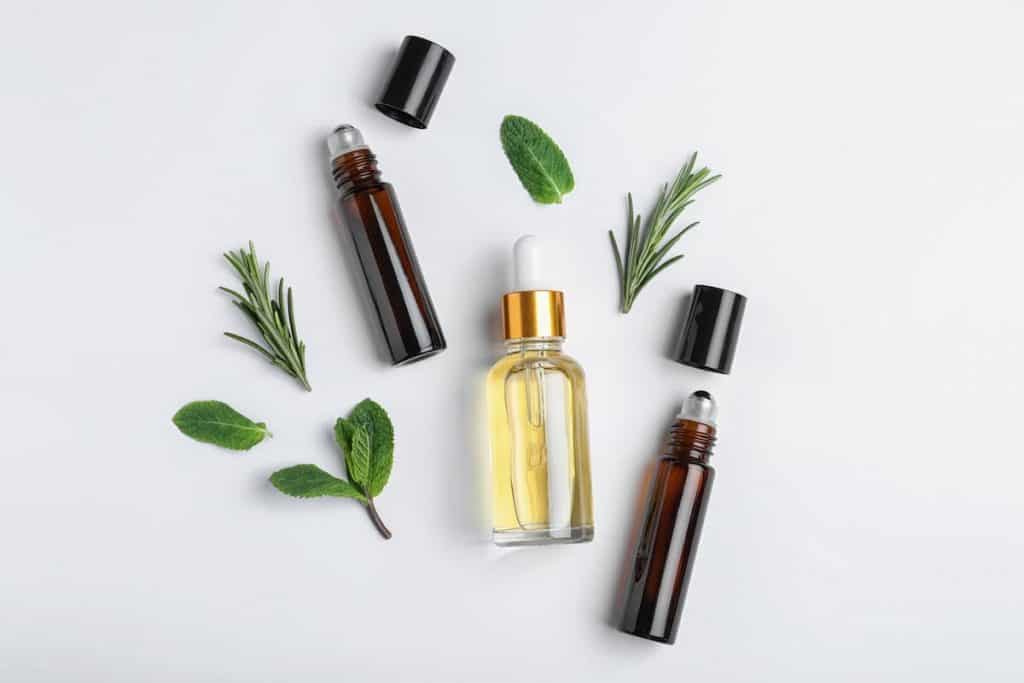essential oil roller bottles and droppers on a white background with greenery