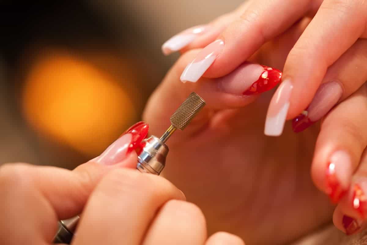 Manicurist with a nail file doing a french manicure on acrylic nails