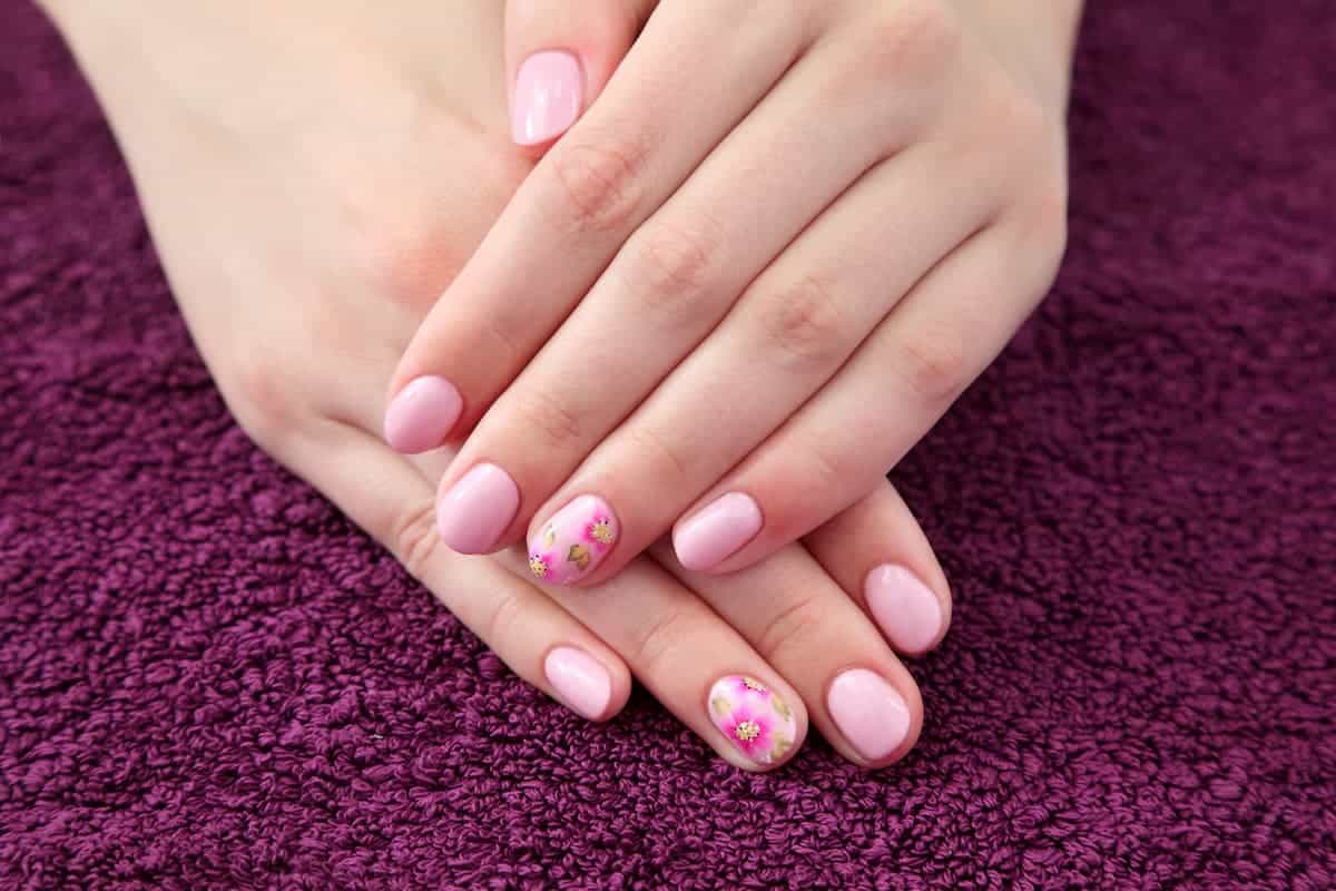 woman's hands folded with light pink floral acrylic nail overlay
