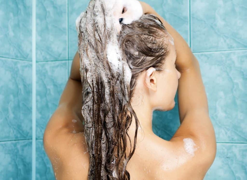woman washing hair with shampoo in a shower with blue tiles