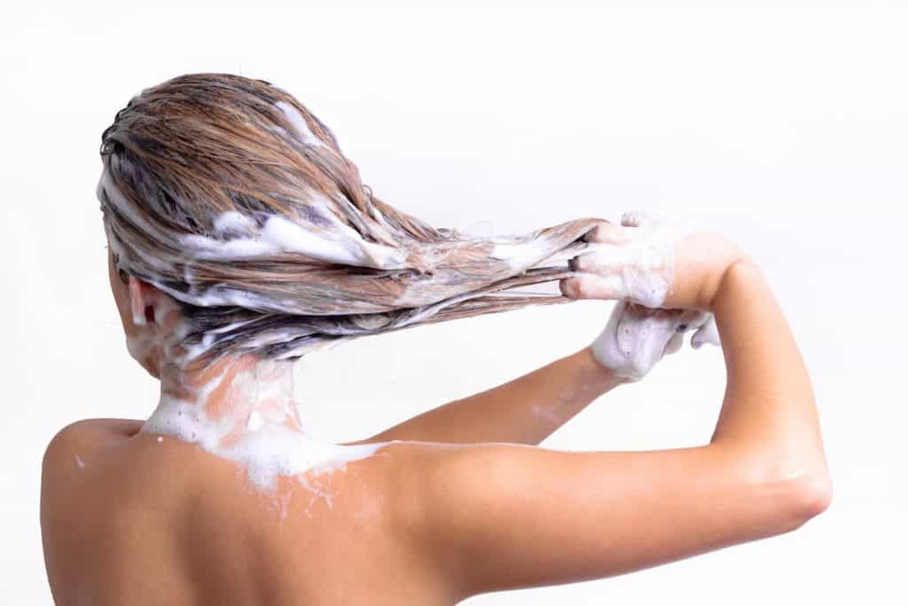 Woman with long hair washing her hair with shampoo