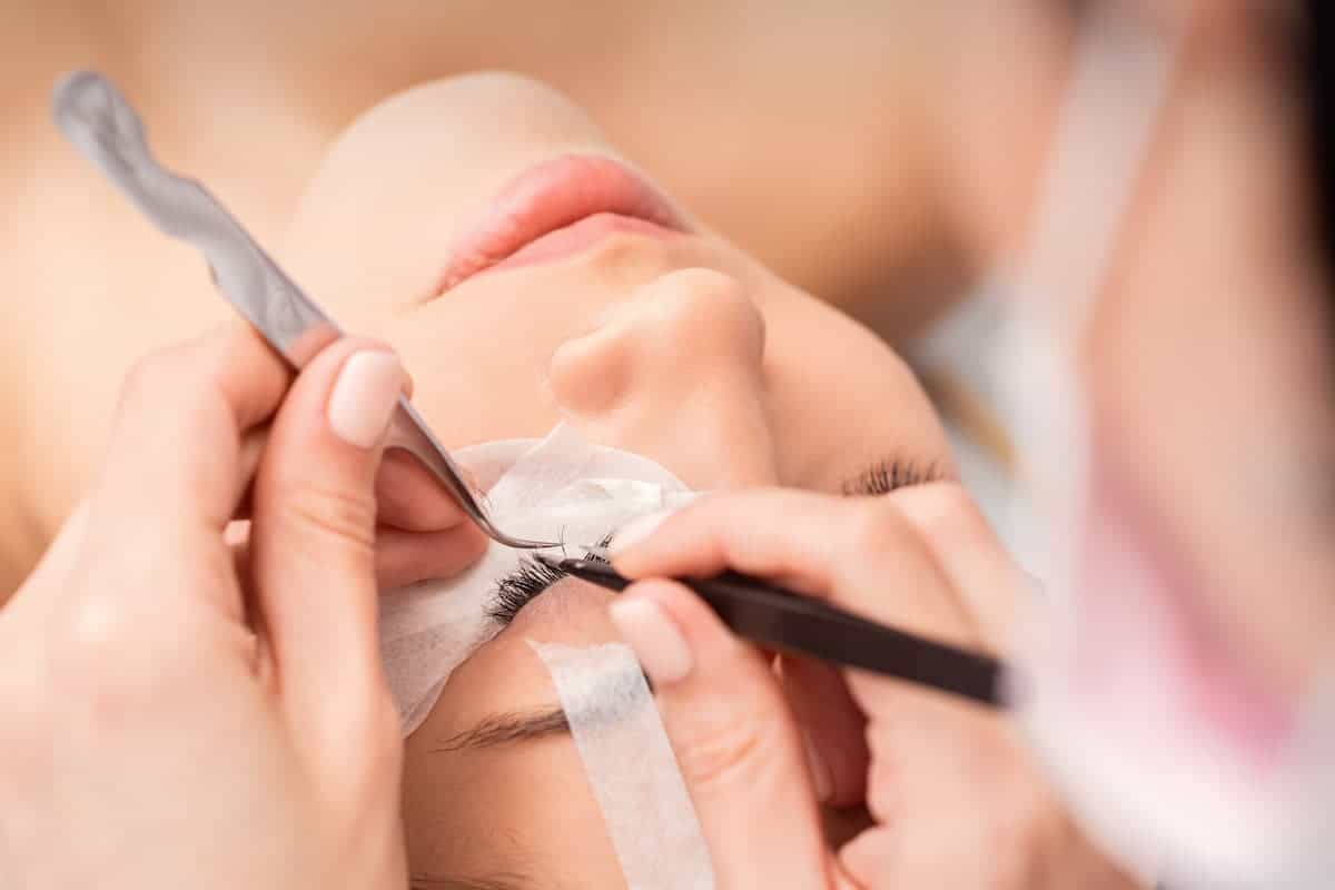 Woman having eyelash extensions applied by a lash artist