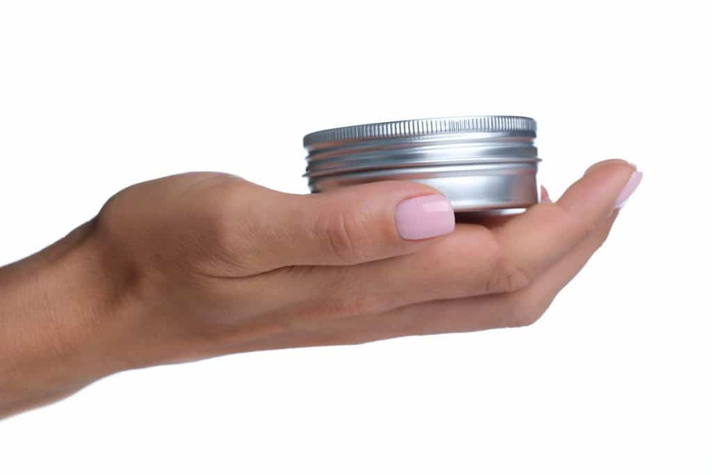 manicured hand holding a silver container of cleansing balm