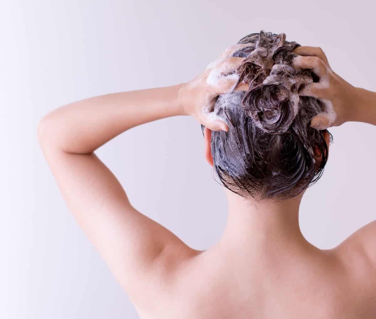 woman with dark hair washing hair with shampoo