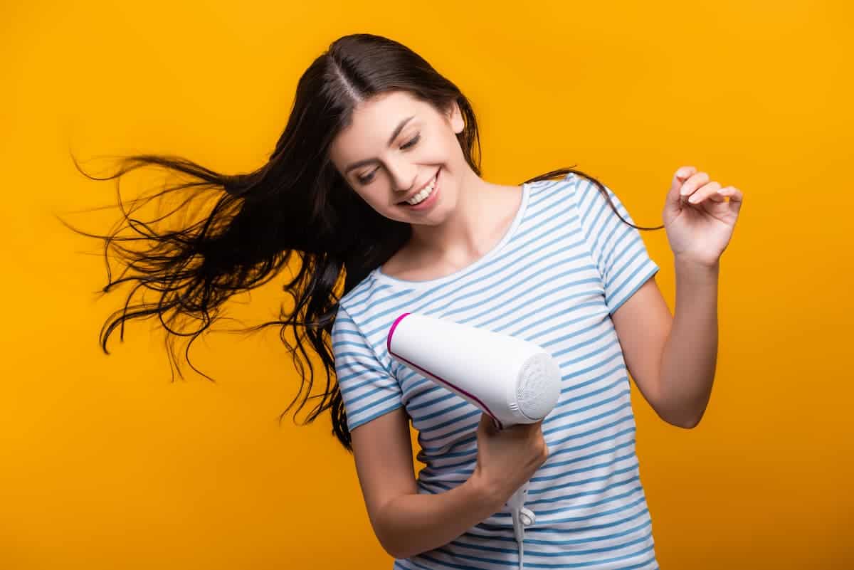 Brunette woman holding a white hair dryer on a yellow background