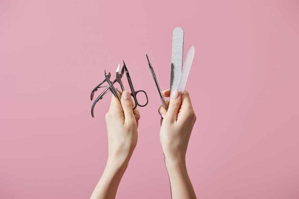 woman holding up manicure tools like scissors and cuticle nippers