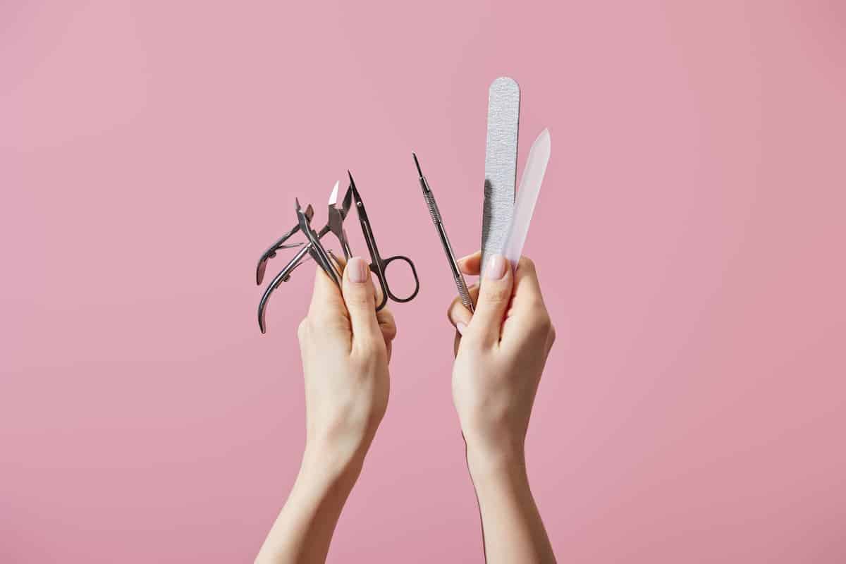 woman holding up manicure tools like scissors and cuticle nippers