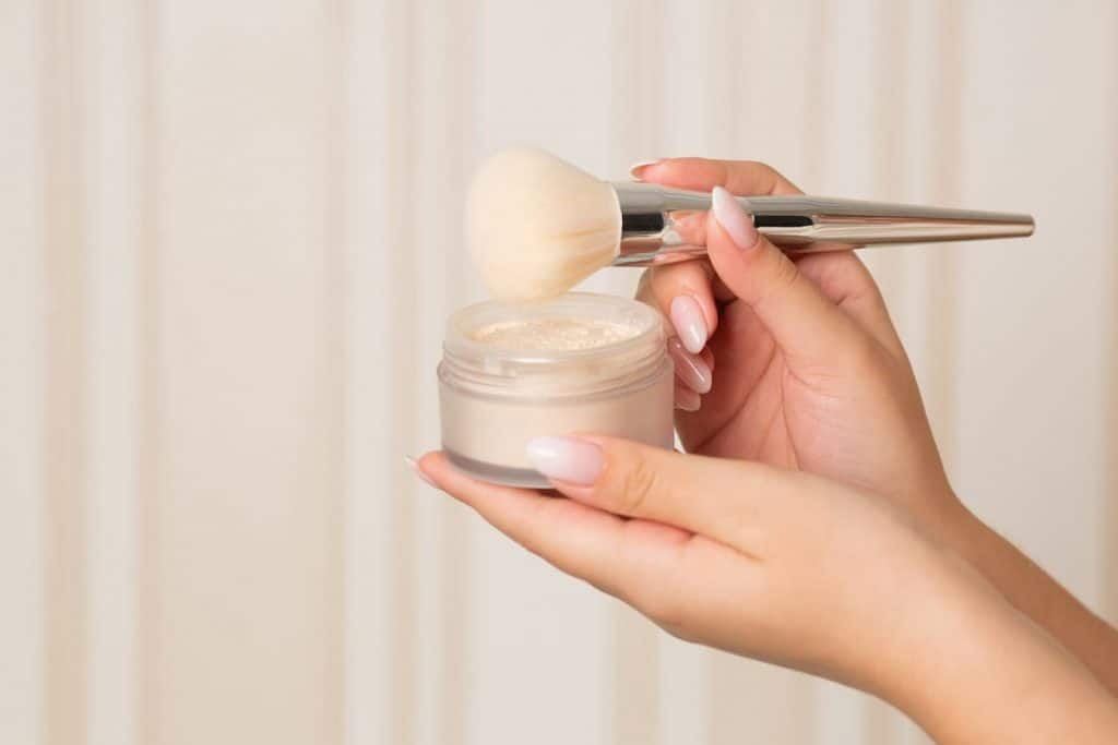 woman with manicured nails holding setting powder and a brush
