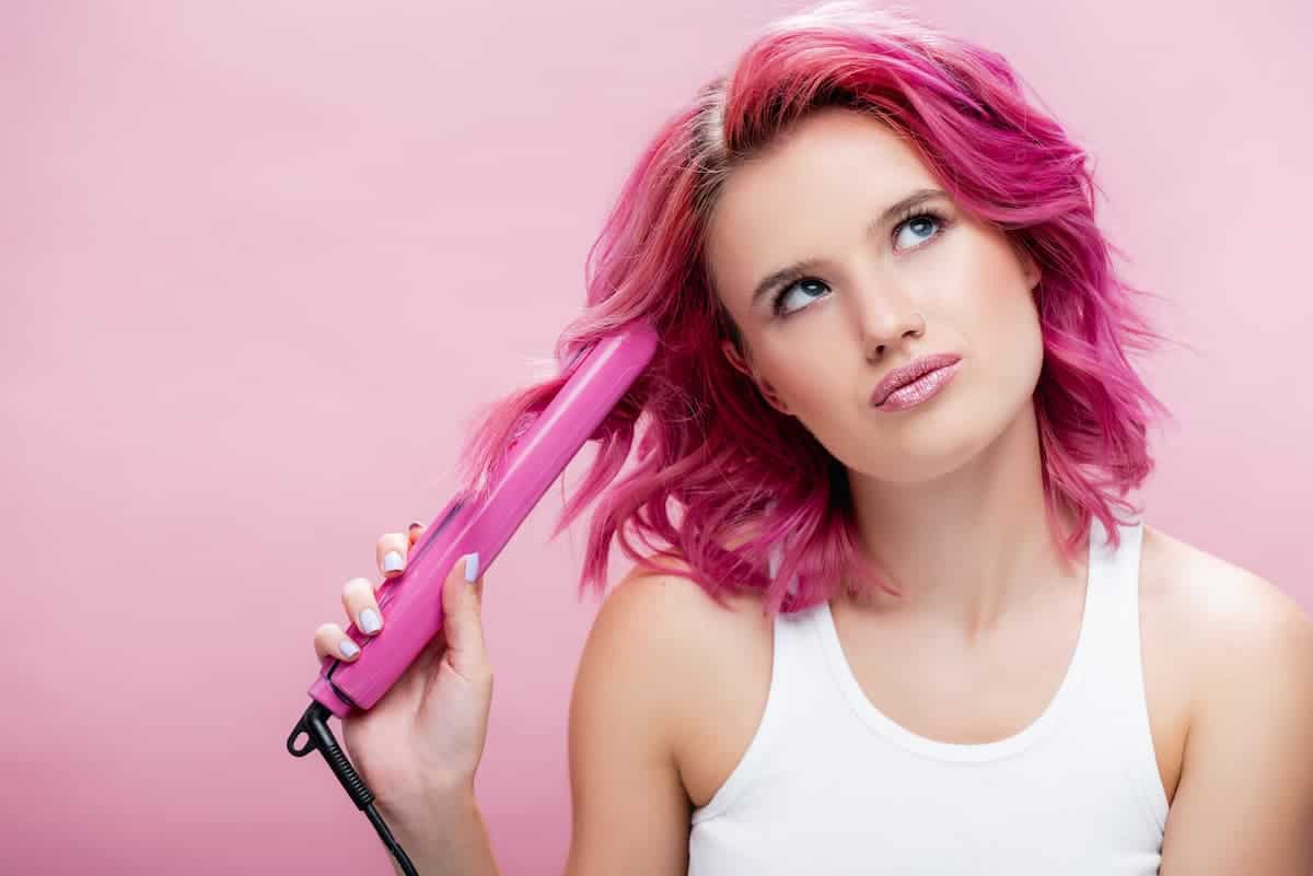 woman with pink hair holding a pink hair straightener
