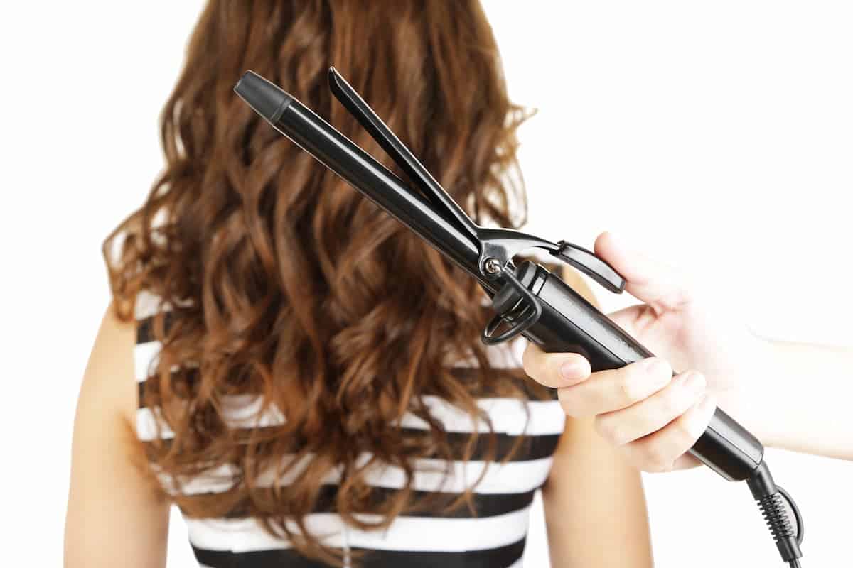 hand holding a curling iron in front of woman with brown curled hair