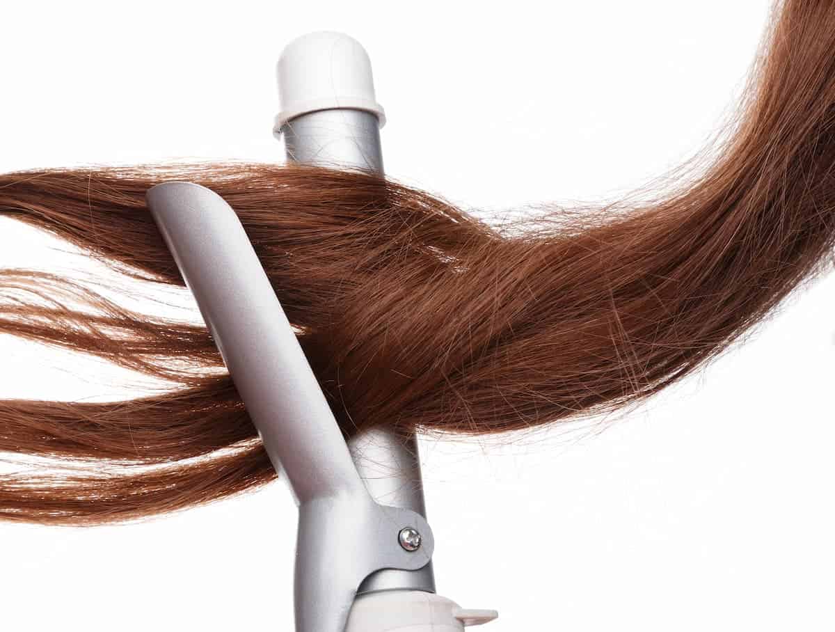 auburn hair being curled by a silver and white ceramic curling iron 