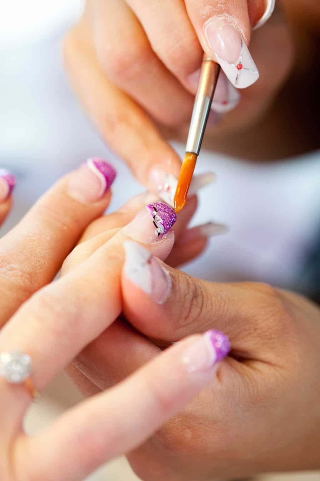 manicurist applying acrylic polish to fingernails with a nail brush
