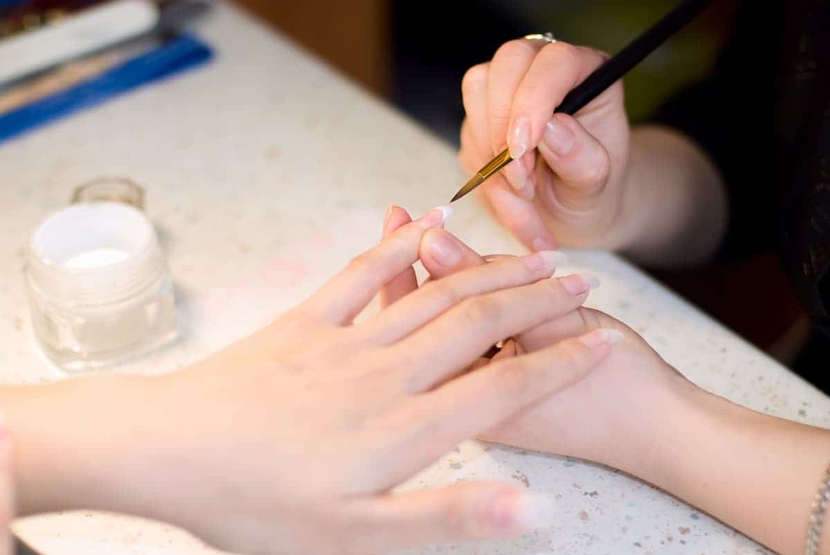 manicurist using a nail brush to apply acrylic nails