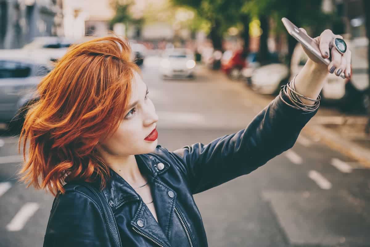 Woman with copper colored hair taking a selfie in the middle of the street