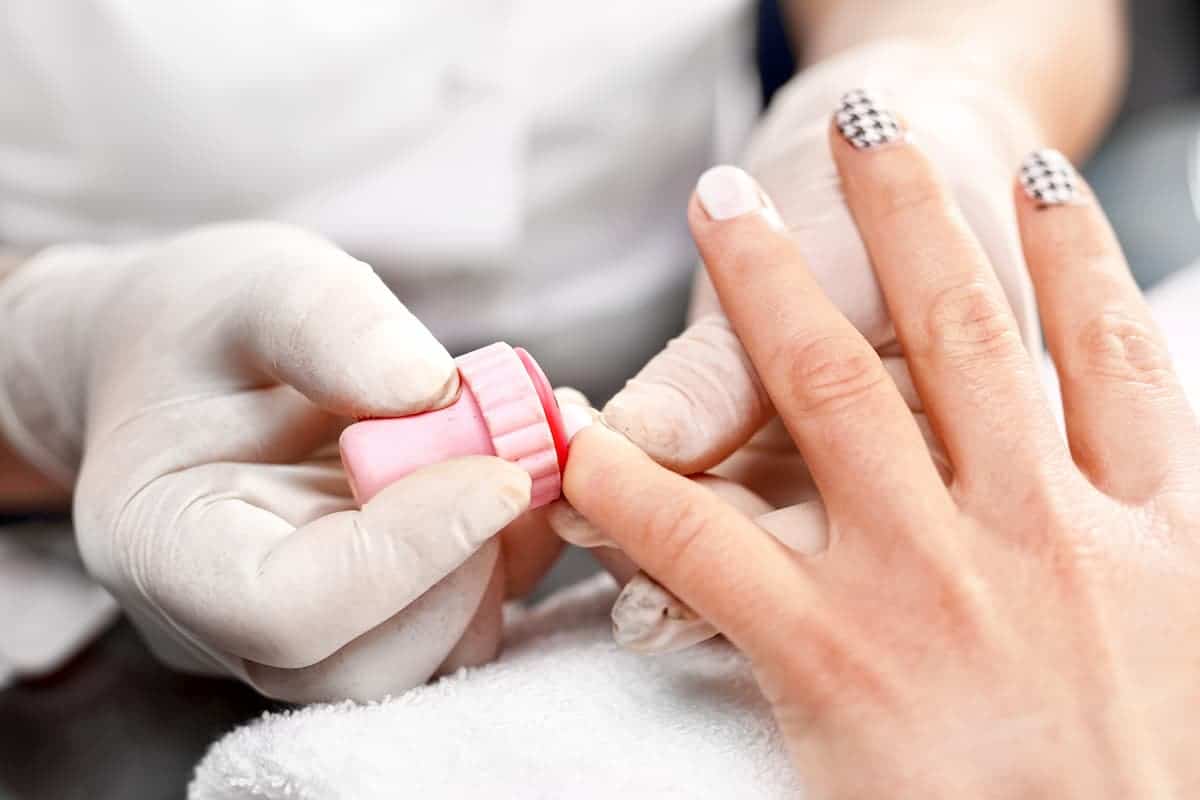 manicurist using a stamping tool to apply nail design to white finger nail