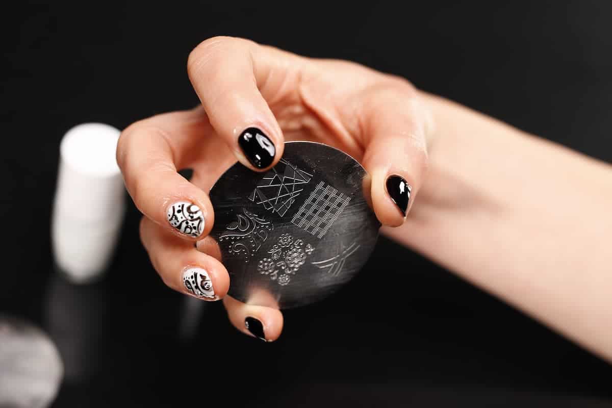 hand with black and white designs on finger nails holding a nail polish stamping plate