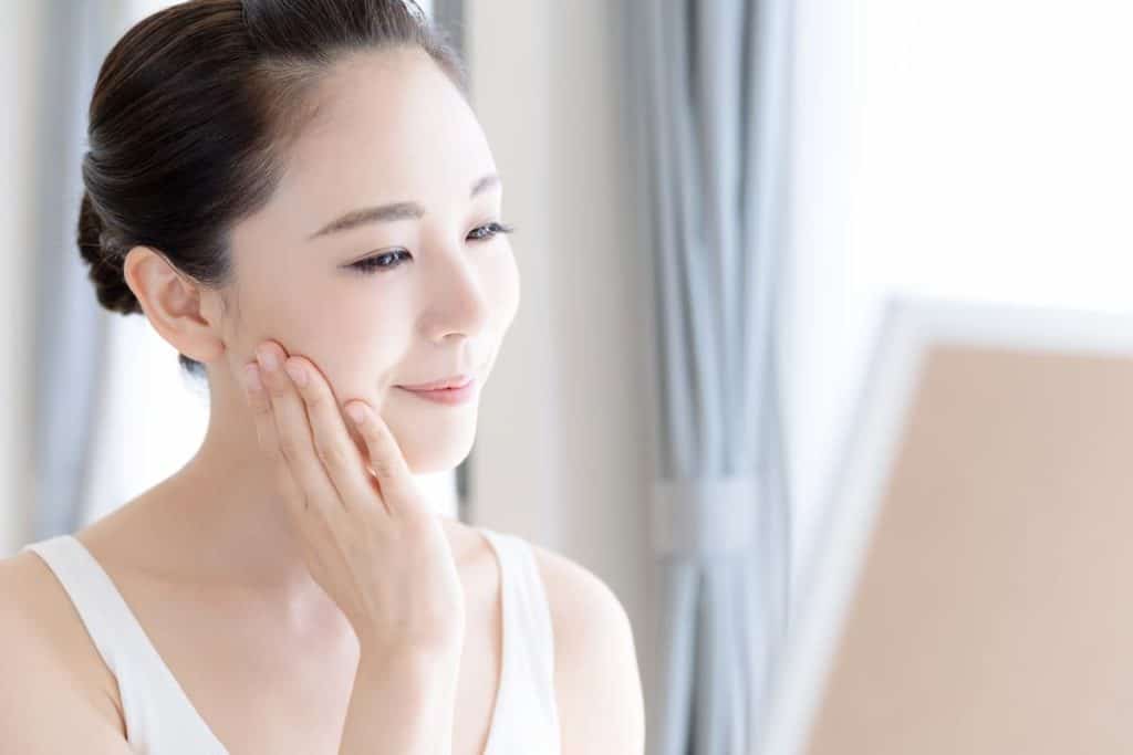 A woman is applying the best Korean toner to her face in front of a mirror.