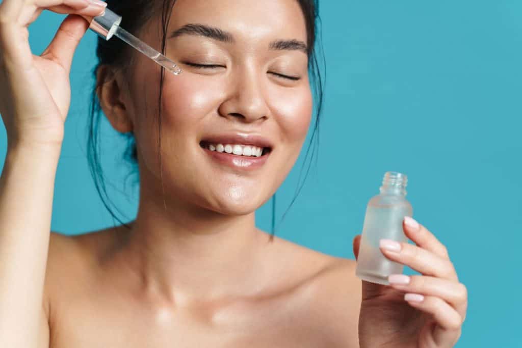 image of an asian girl applying facial serum isolated over blue background
