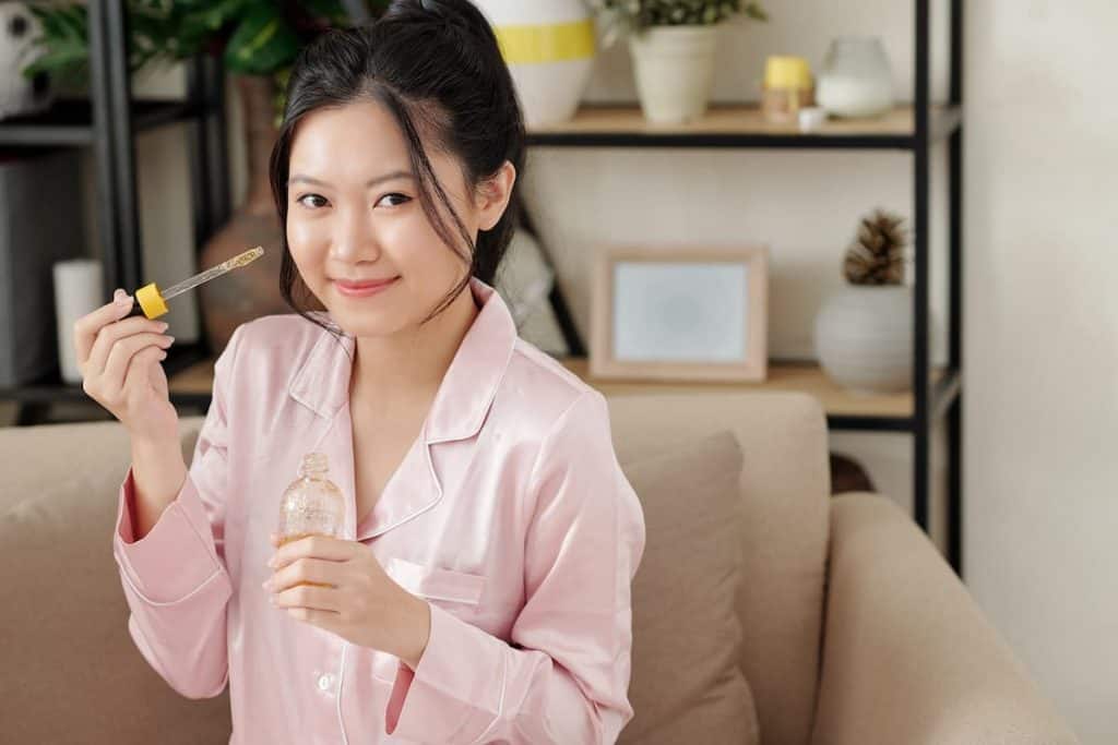 pretty smiling young woman applying serum with vitamin c on her face before going to bed
