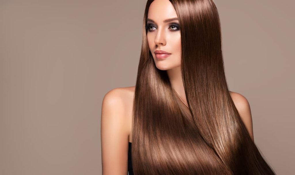 A beautiful woman with long brown hair posing on a brown background after a keratin treatment