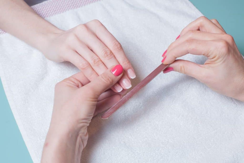 nail technician filing woman's fingernails with a solar nail or french tip manicure
