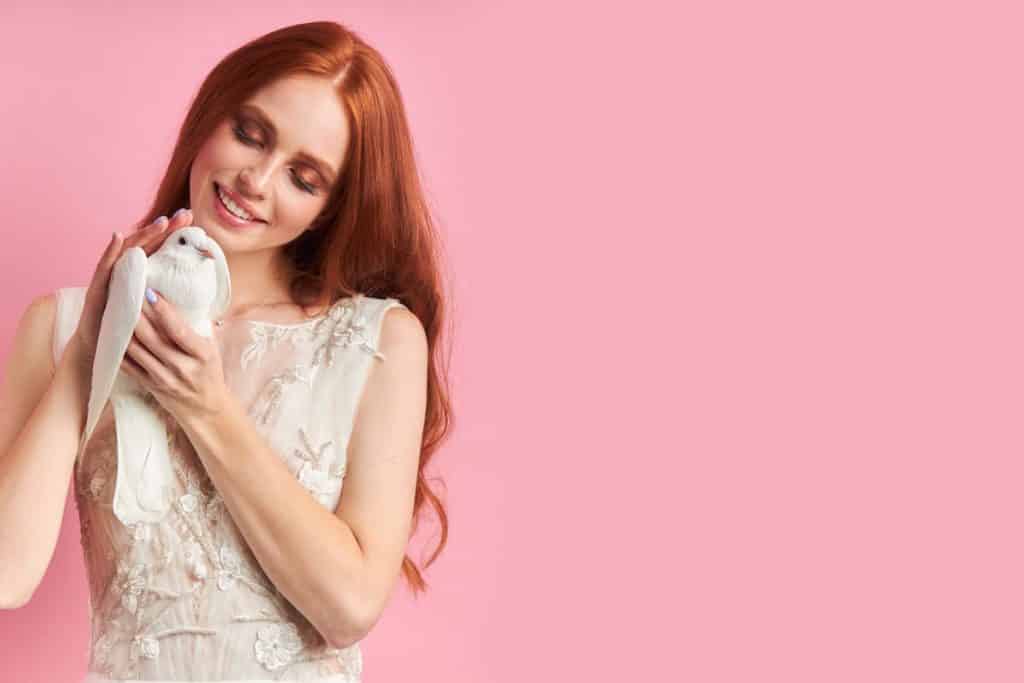 Young female with red auburn hair in white dress holding white dove