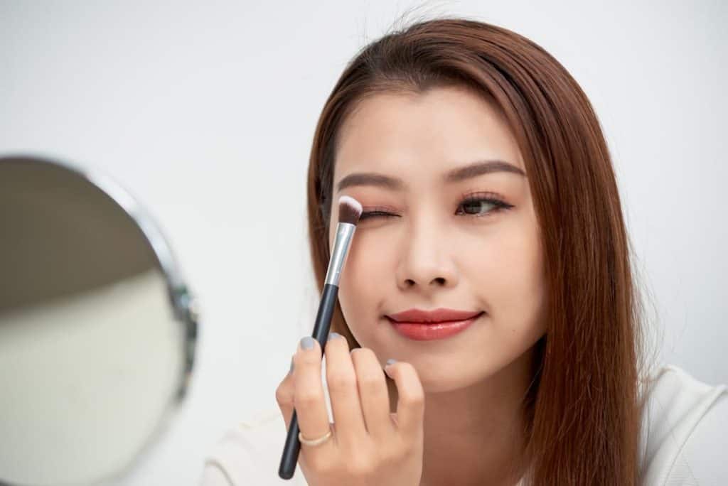 Asian woman applying eyeshadow on eyebrow with brush