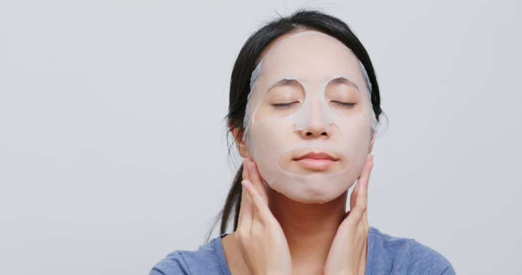 Asian woman in blue shirt applying face mask sheet