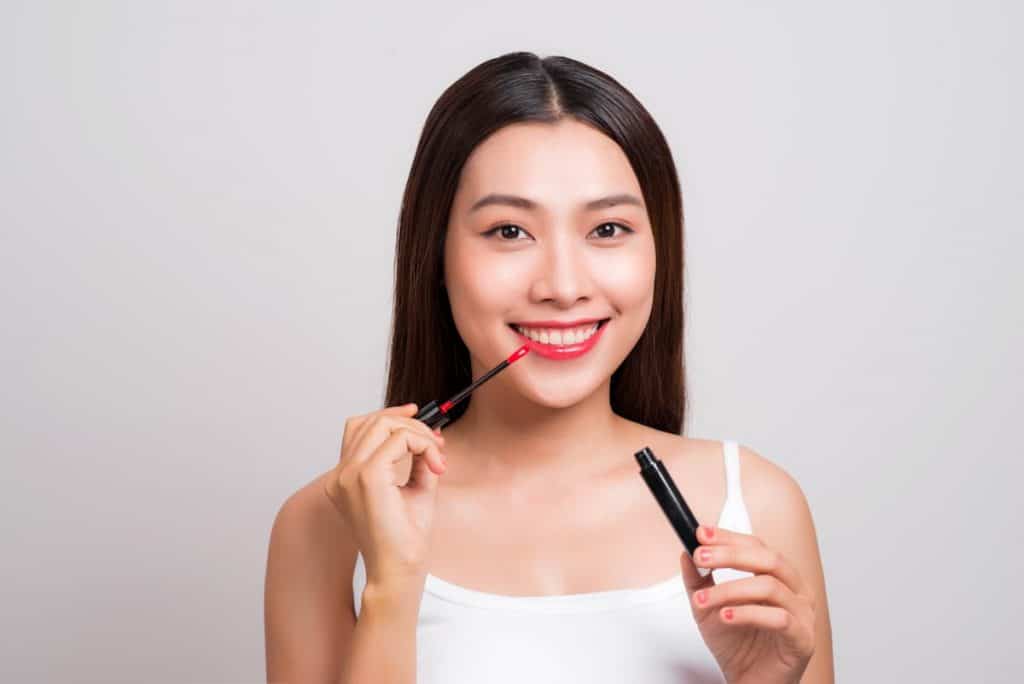 Asian woman white spaghetti strap tops applying red lip tint