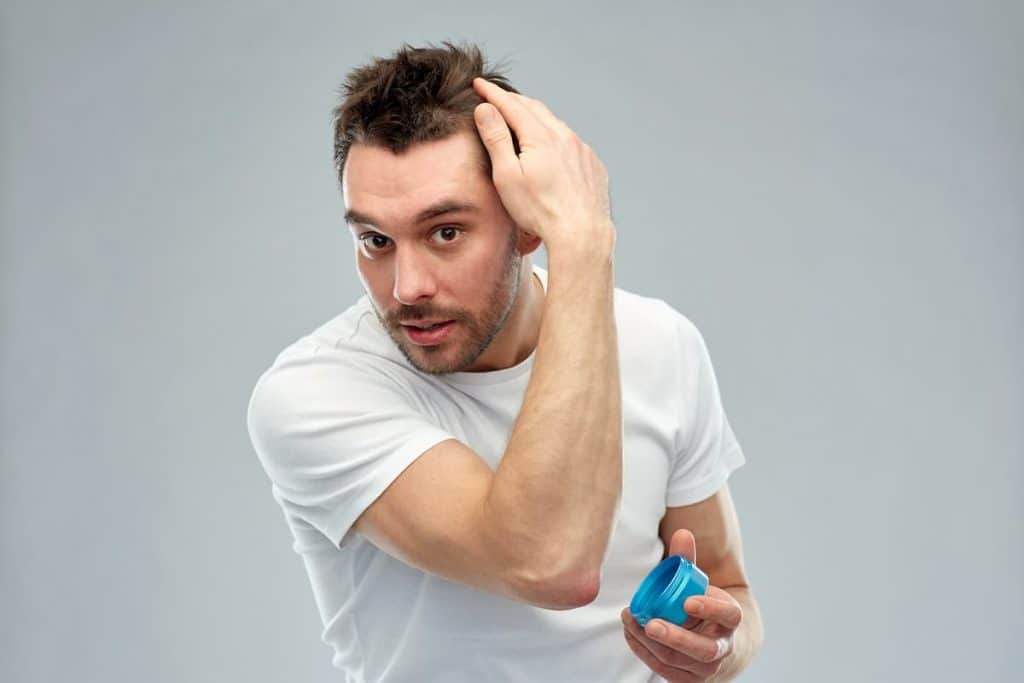man wearing white shirt styling his hair with wax