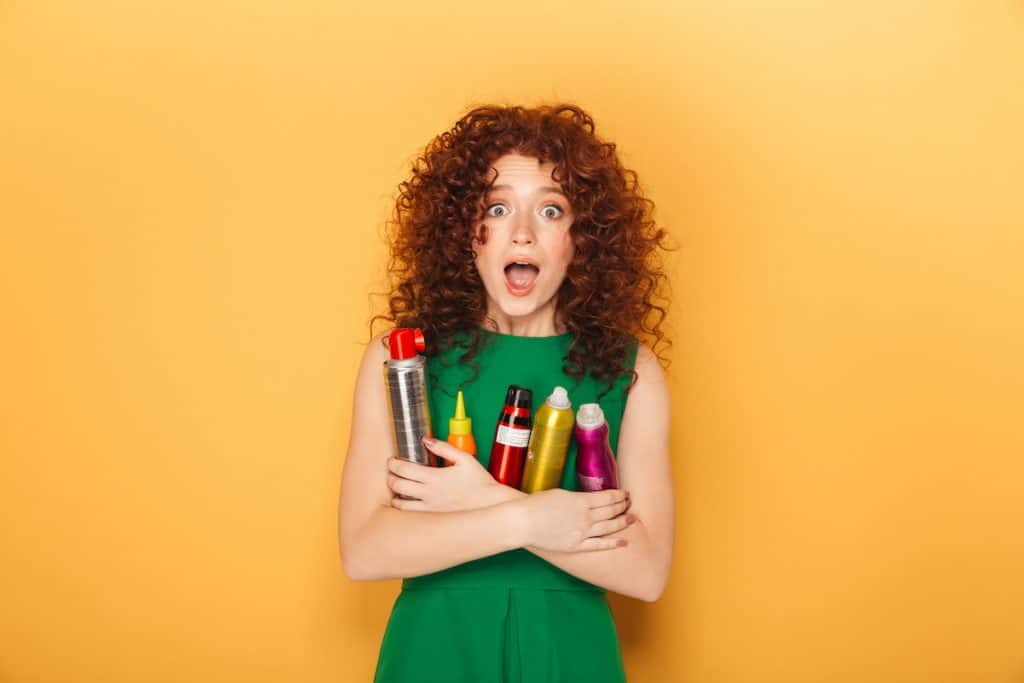 curly-redhaired woman with a surprised expression on her face holding hair products