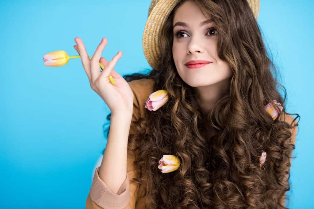 beautiful curly-haired lady wearing a hat holding tulips in a lightblue background