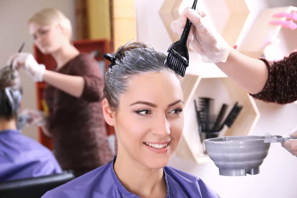 hairdresser applying hair dye on woman's hair
