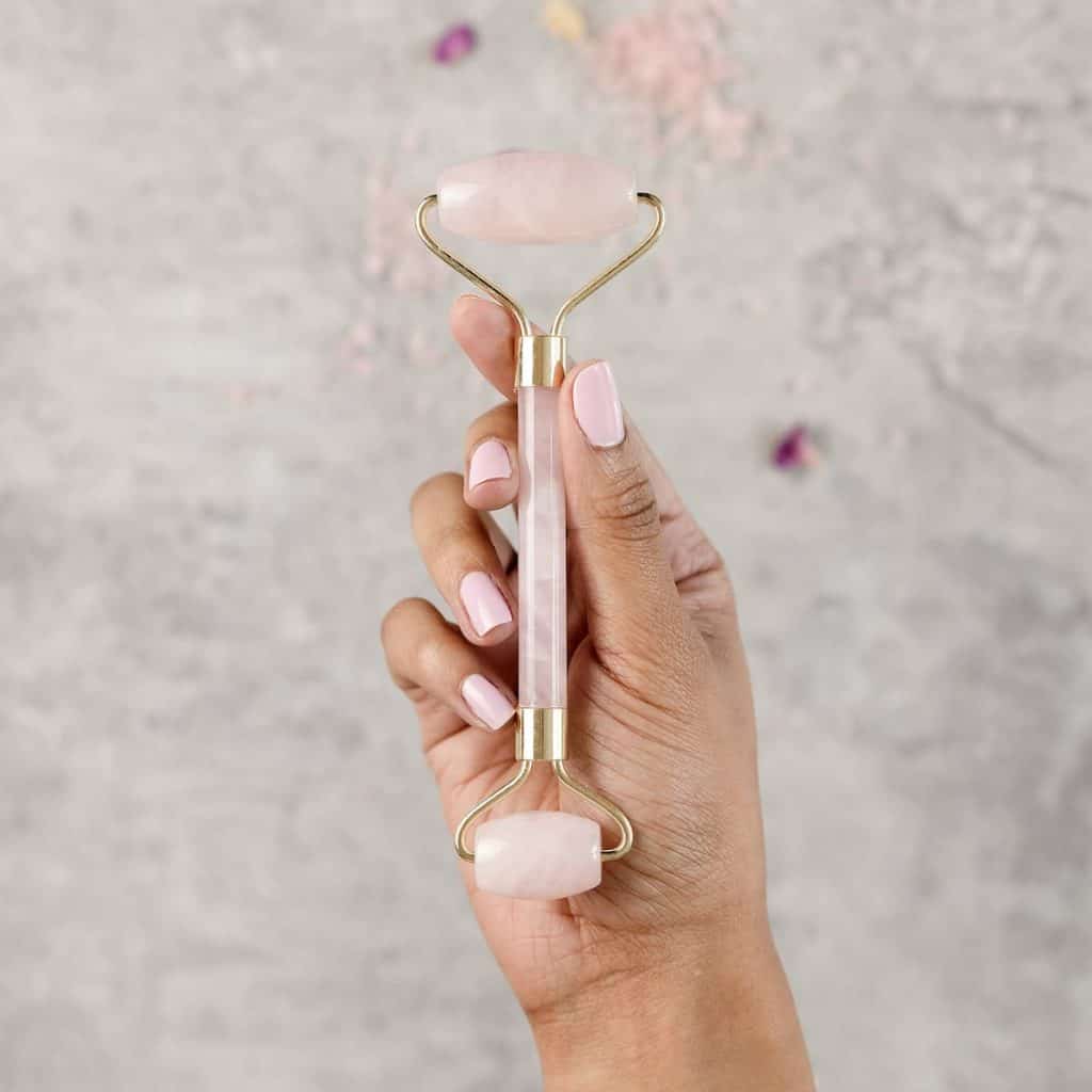 hand with pink nails holding a rose quartz roller in a portrait with gray marbled background