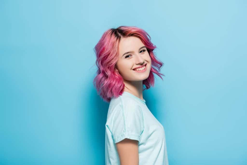 side view of young woman with pink hair smiling on blue background