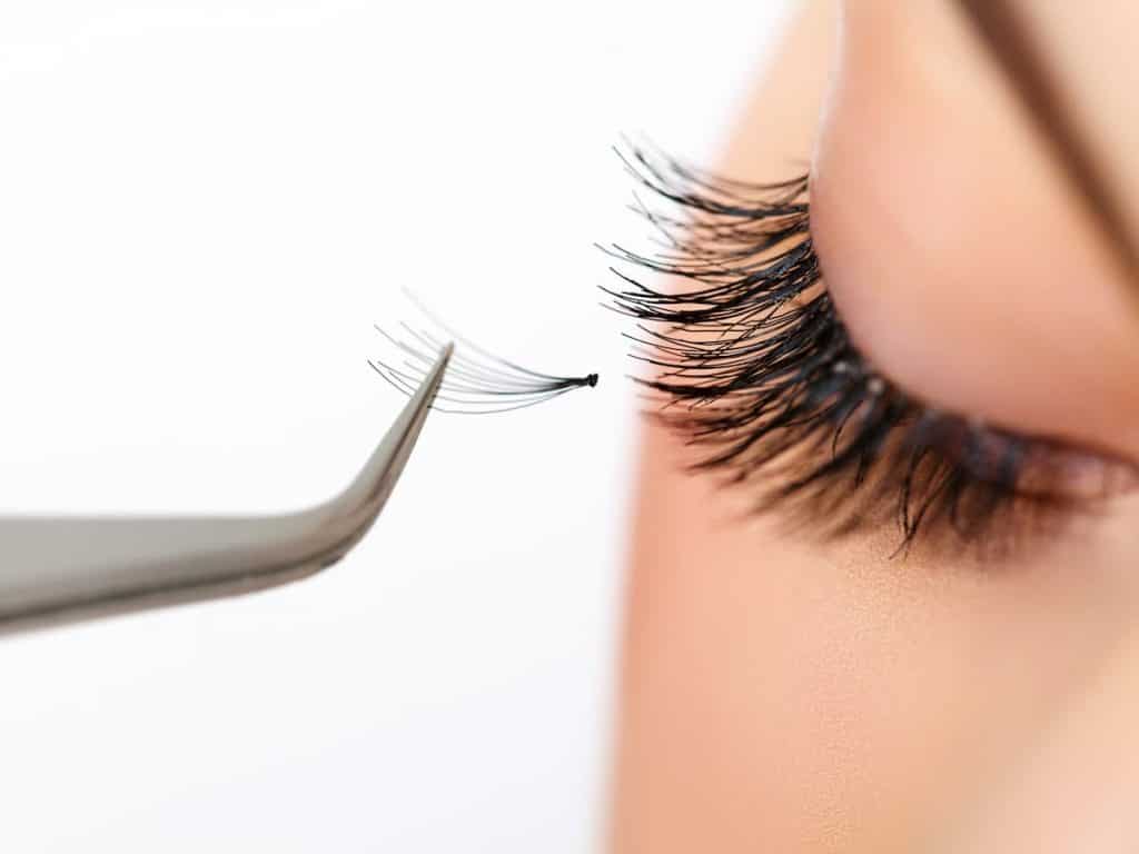 tweezers with a false eyelash extension near the eyelashes of a woman