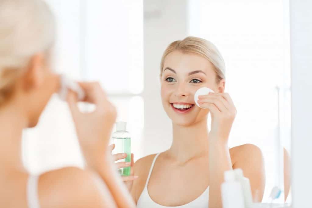 Young woman with micellar water washing face at bathroom