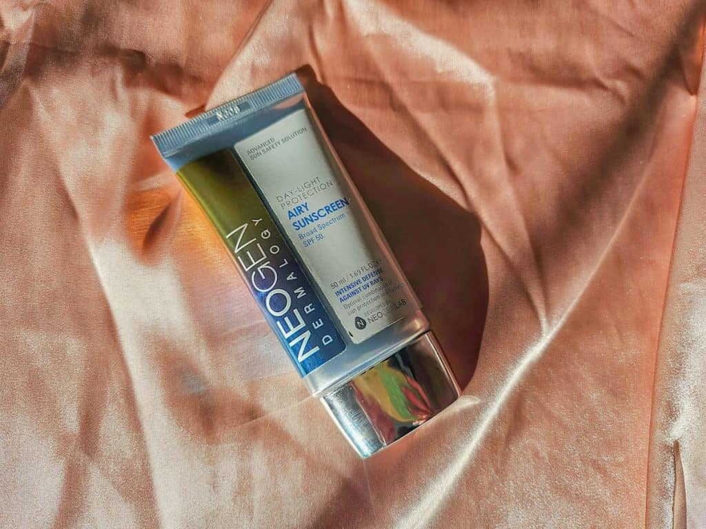 A tube of neogen airy sunscreen on pink satin sheet
