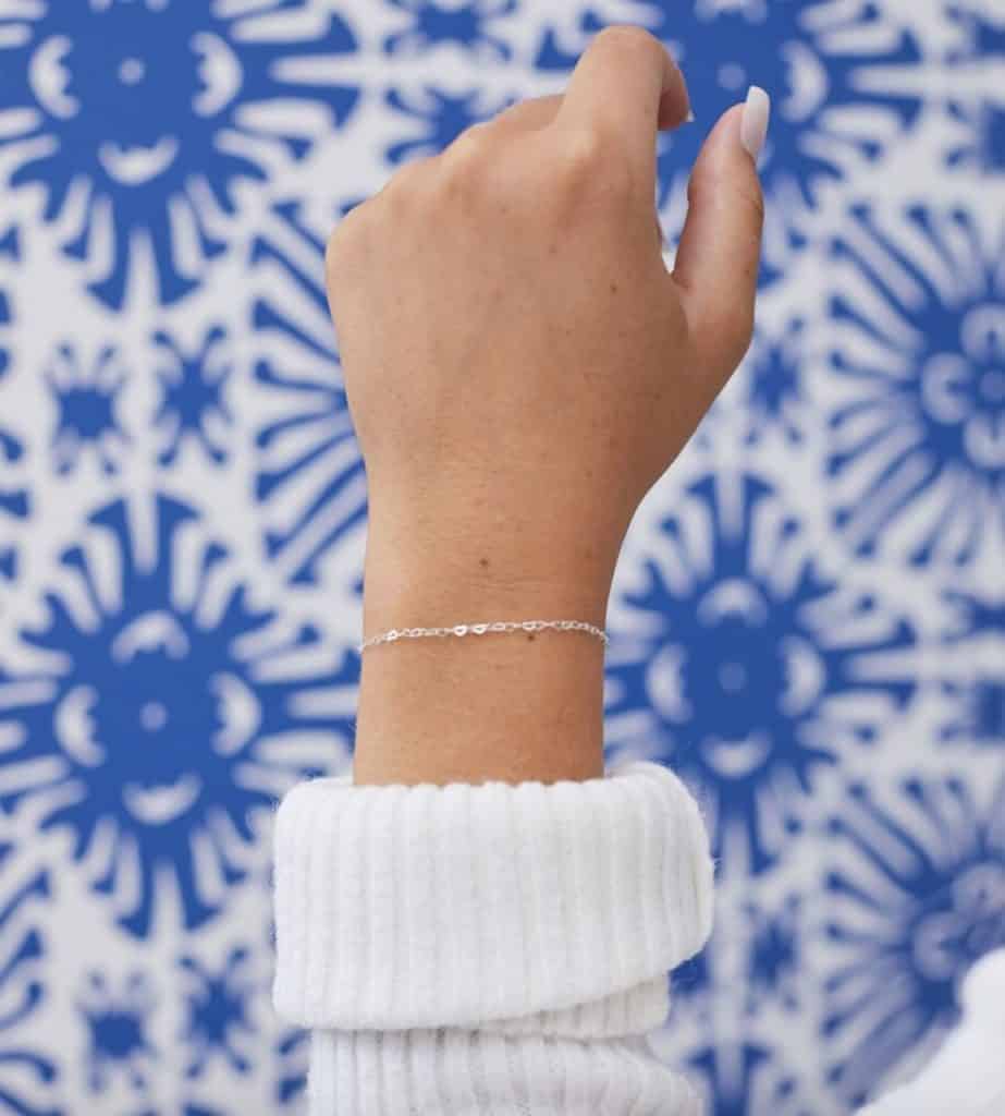 arm with silver permanent jewelry bracelet with a blue and white background