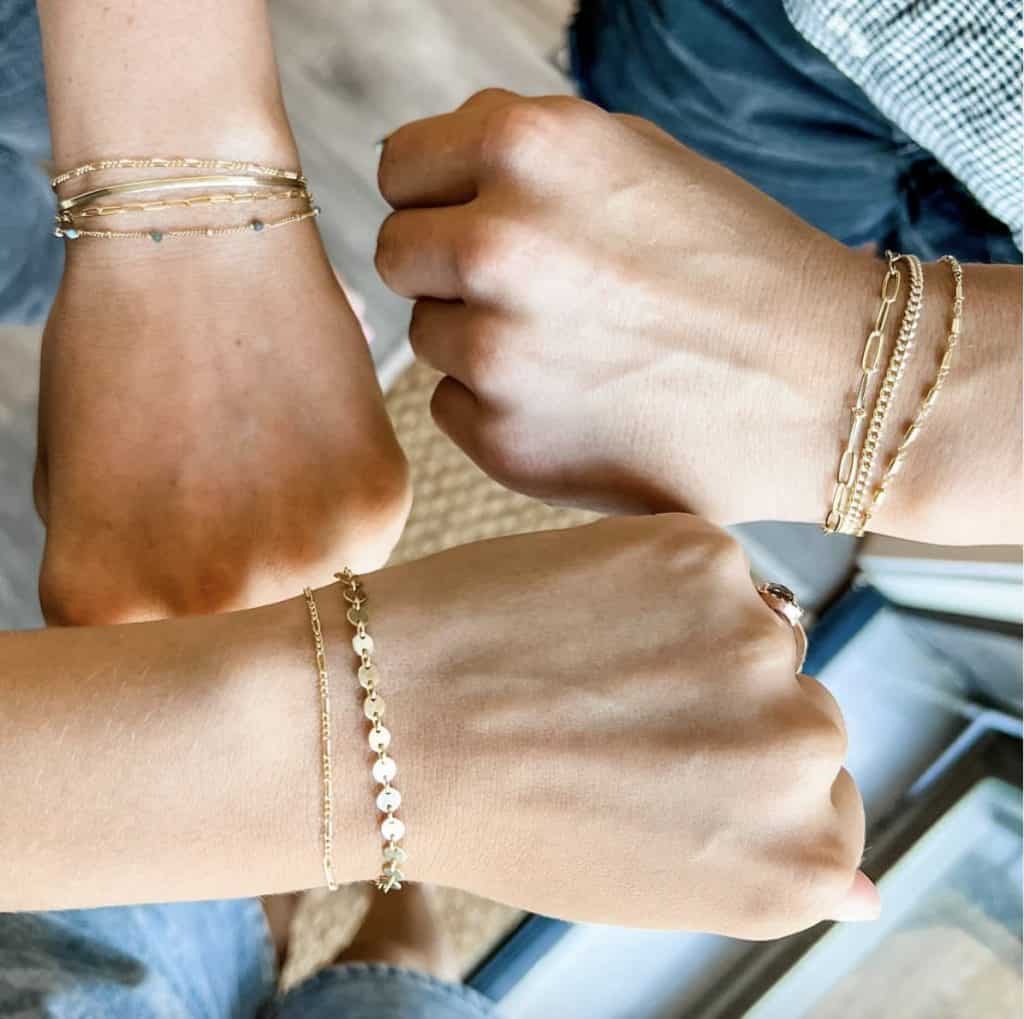 three arms with hands in fists with gold permanent jewelry bracelets