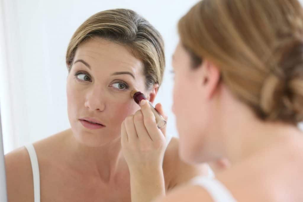 Woman applying concealer around eyes